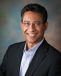 Smiling man in a suit against a backdrop.