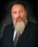 Bearded man in formal attire, serious expression.